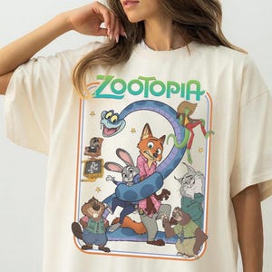 以下が含まれることがあります： アイボリー色のTシャツ。映画「ズートピア」のカラフルなグラフィックが特徴です。「ズートピア」のタイトルは緑色で、青いヘビと漫画のキャラクターが描かれています。半袖でゆったりとしたフィット感です。