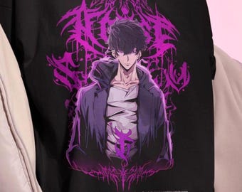 May include: Black t-shirt featuring a purple anime-style illustration of a character in a hooded jacket. The graphic includes intricate design elements and text at the bottom. The shirt is worn by a person.