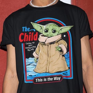 K&ouml;nnte beinhalten: Schwarzes T-Shirt mit einer Grafik von "The Child" aus Star Wars. Das Design enth&auml;lt den Text "The Child" in Rot, "Caring for your Unexpected Bounty" und "This is the Way" in Wei&szlig;.