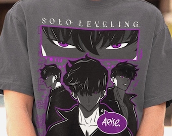 May include: Dark gray t-shirt featuring a graphic from the anime series "Solo Leveling." The design includes the text "Solo Leveling" above a purple-framed image of eyes and a character with the word "Arise" in a speech bubble.