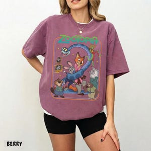 以下が含まれることがあります： ベリー色のTシャツ。映画「ズートピア」のカラフルなグラフィックが特徴です。ジュディ・ホップスやニック・ワイルドなどのキャラクターが描かれ、緑色の「Zootopia」の文字があります。クルーネックで半袖です。
