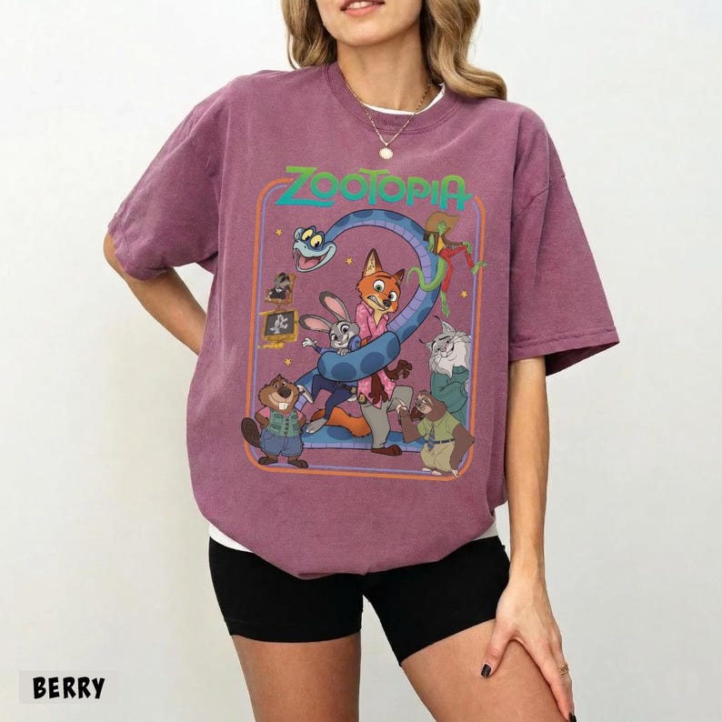 以下が含まれることがあります： ベリー色のTシャツ。映画「ズートピア」のカラフルなグラフィックが特徴です。ジュディ・ホップスやニック・ワイルドなどのキャラクターが描かれ、緑色の「Zootopia」の文字があります。クルーネックで半袖です。