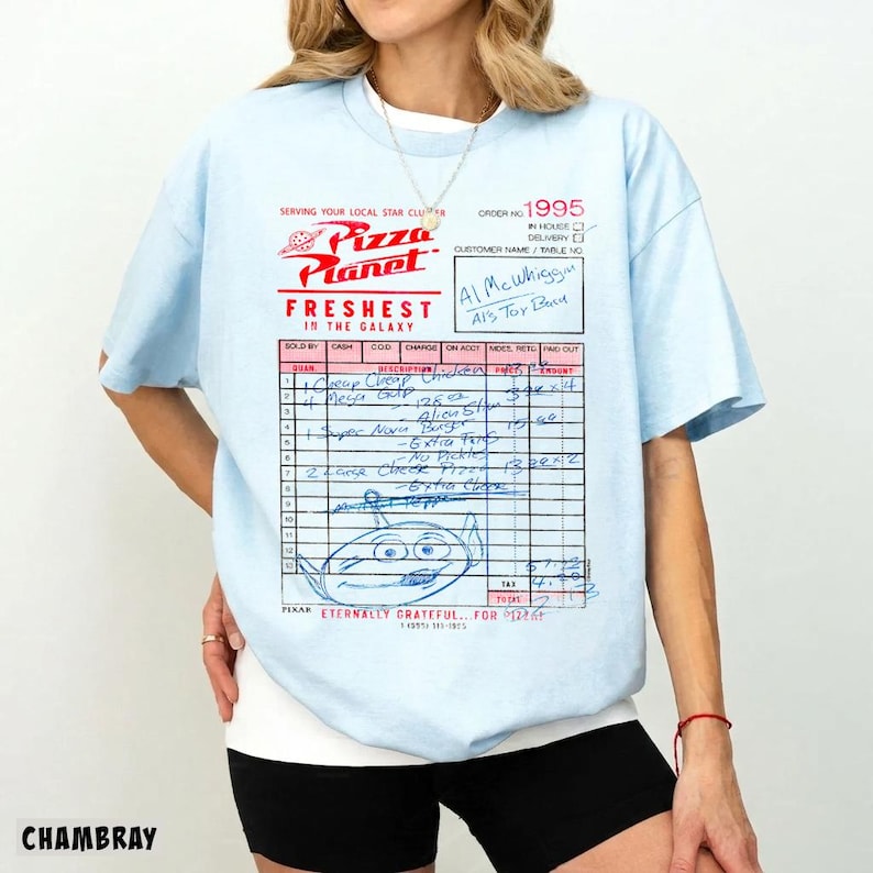 Puede incluir: Camiseta azul claro con un dise&ntilde;o de recibo de Pizza Planet. El gr&aacute;fico incluye el logotipo de Pizza Planet, texto y un dibujo de un extraterrestre. La camiseta tiene mangas cortas y cuello redondo.