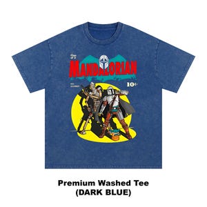 May include: Dark blue premium washed tee featuring a comic book style graphic of The Mandalorian and another character. The graphic includes the word "MANDALORIAN" in red, a yellow background, and the text "Clan of 2".