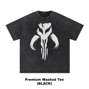 May include: Black washed tee shirt with a white graphic design. The graphic is a stylized symbol with curved lines and vertical strokes. The text at the bottom reads "Premium Washed Tee (BLACK)".