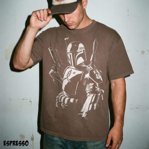 May include: Espresso-colored t-shirt featuring a white graphic of a character with a helmet, holding a blaster and a spear. The word "ESPRESSO" is printed at the bottom. The shirt is a casual wear item.