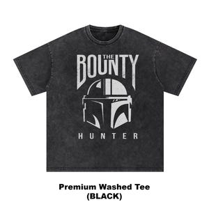 Puede incluir: Camiseta negra lavada de primera calidad con un gr&aacute;fico blanco de un casco y las palabras "THE BOUNTY HUNTER". La camiseta tiene cuello redondo y mangas cortas. El texto "Premium Washed Tee (BLACK)" est&aacute; en la parte inferior.