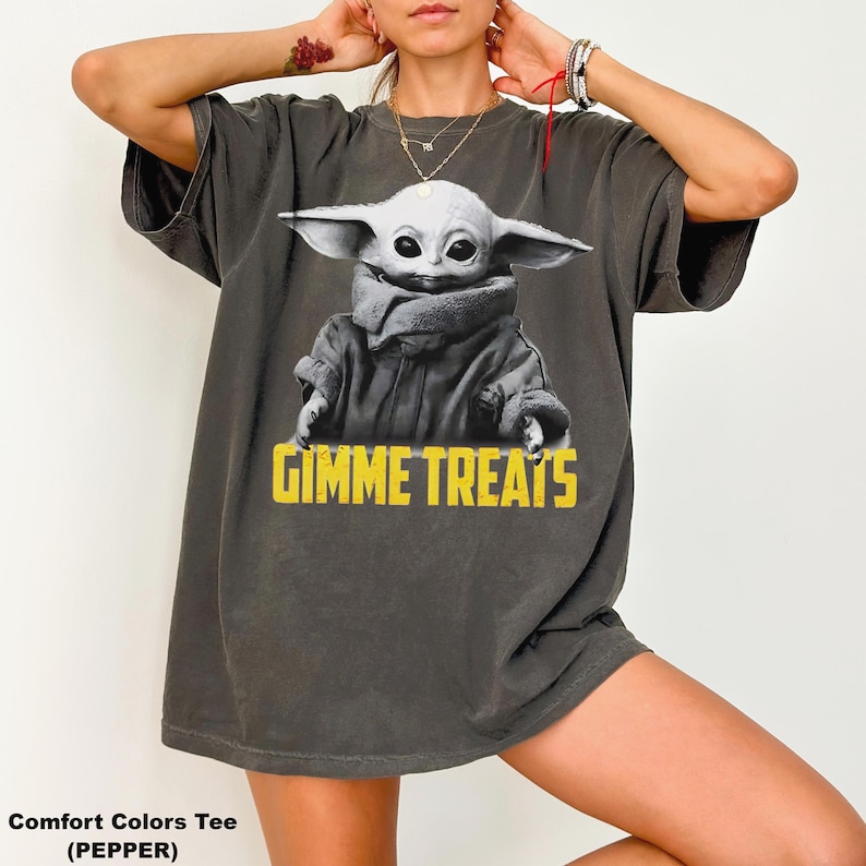 Op de afbeelding: Donkergrijs Comfort Colors T-shirt met een afbeelding van een personage met grote oren en de tekst "GIMME TREATS" in het geel. Het T-shirt heeft een relaxte pasvorm.