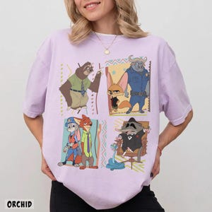 Puede incluir: Camiseta lila claro con un gr&aacute;fico de dibujos animados colorido de personajes de Zootopia. La palabra "ORCHID" est&aacute; impresa en la parte inferior. La camiseta tiene mangas cortas y cuello redondo.
