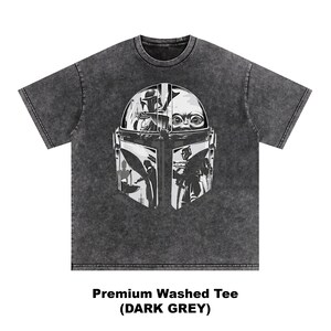 May include: Dark grey, washed t-shirt with a large black and white graphic of a Mandalorian helmet and Grogu. The text at the bottom reads "Premium Washed Tee (DARK GREY)".