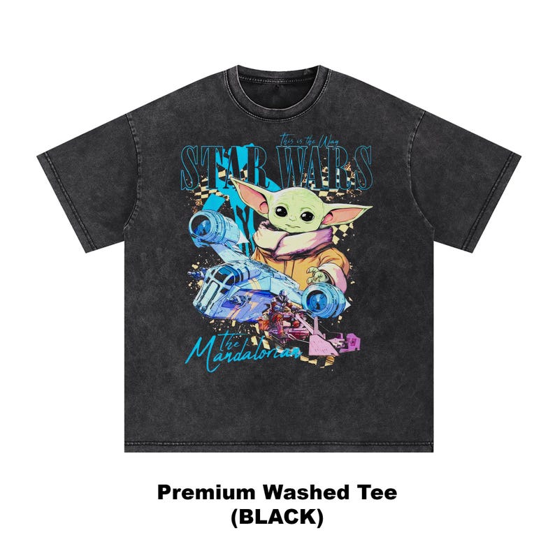 May include: Black washed tee featuring a graphic of Grogu from The Mandalorian, with the text "STAR WARS" and "The Mandalorian". The design includes a spaceship and Grogu in a tan and pink outfit. The shirt has a crew neck.