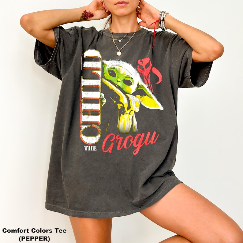May include: Dark gray Comfort Colors tee featuring a graphic of Grogu, also known as The Child, from the Star Wars series. The design includes the word "CHILD" vertically and "Grogu" in red. The shirt has short sleeves.