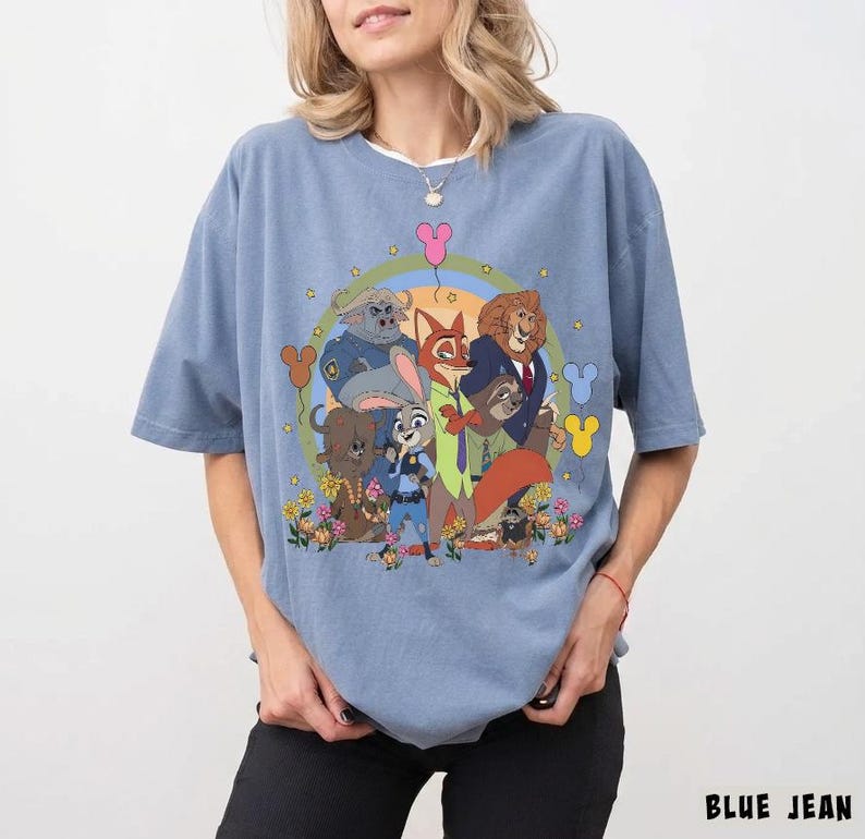 May include: A light blue t-shirt featuring a colorful graphic of characters from the animated movie Zootopia. The design includes Judy Hopps, Nick Wilde, and other characters, surrounded by flowers and Mickey Mouse-shaped balloons. The text "BLUE JEAN" is at the bottom.