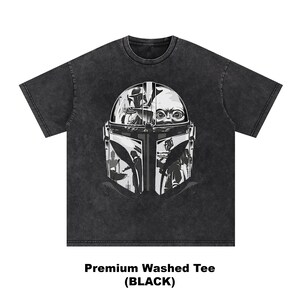 May include: Dark grey washed tee with a graphic of a helmet and a baby's face. The text "Premium Washed Tee (BLACK)" is at the bottom. The shirt is a dark grey colour.