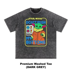 May include: Dark grey t-shirt featuring a graphic of Grogu from Star Wars. The design includes the text "STAR WARS DON'T PUSH MY BUTTONS" in a rectangular frame. The shirt is a premium washed tee.