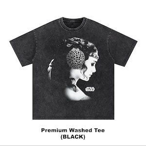 May include: Black washed tee featuring a grayscale portrait of a woman with a decorative headpiece, a profile view, and the Star Wars logo. The text "Premium Washed Tee (BLACK)" is printed at the bottom.