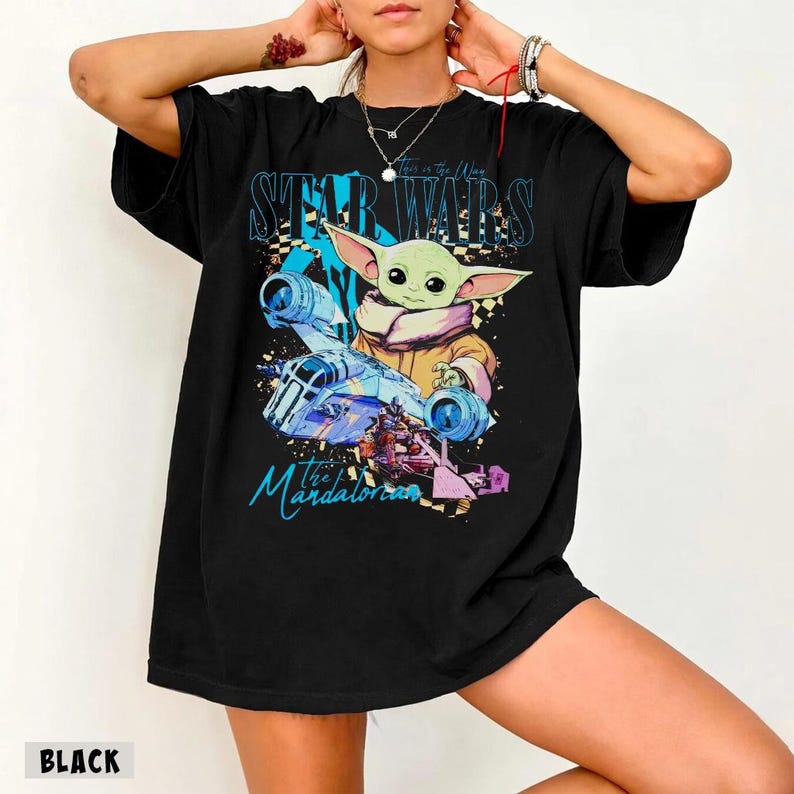 May include: Black t-shirt with a colourful graphic of Grogu from The Mandalorian, with the text "STAR WARS" and "the Mandalorian". The design includes a spaceship and other characters. The word "BLACK" is printed at the bottom.