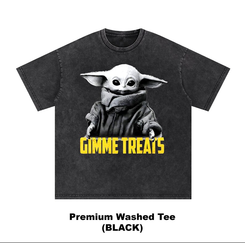 Op de afbeelding: Zwart gewassen T-shirt met een afbeelding van een personage met grote oren en de tekst "GIMME TREATS" in geel. Het personage draagt een jas en heeft een neutrale uitdrukking. Het shirt heeft een ronde hals.