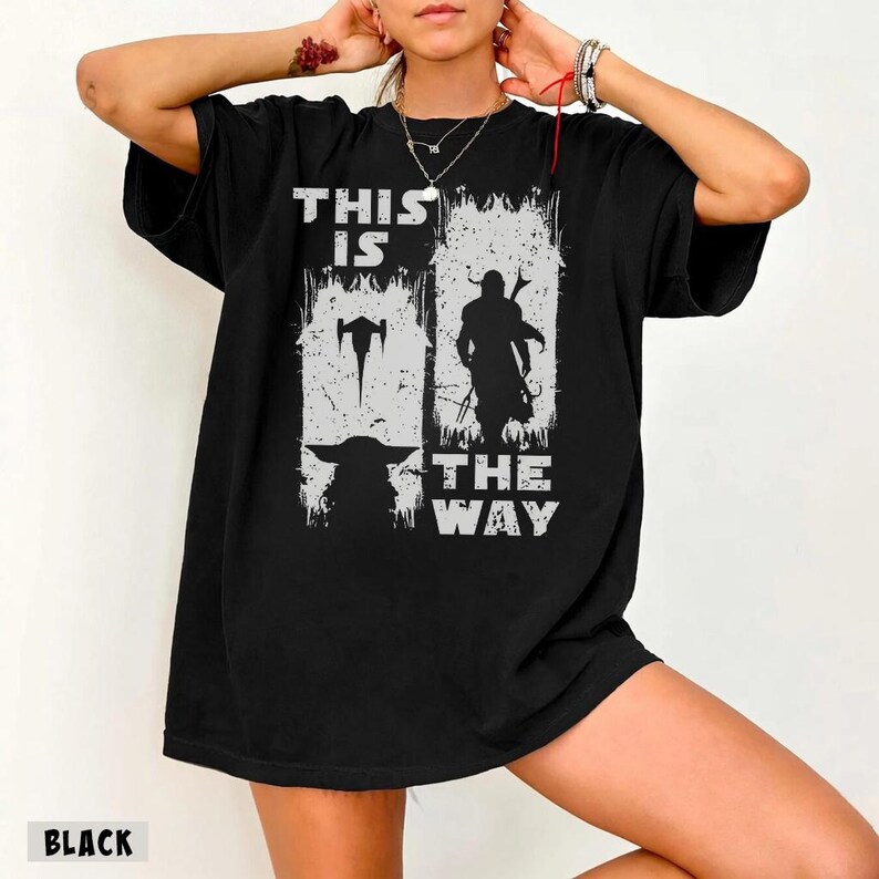 May include: Black t-shirt with a distressed white graphic featuring the text "THIS IS THE WAY" and silhouettes of a character and a creature. The shirt has a crew neck and short sleeves.