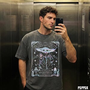 May include: Dark gray t-shirt featuring a graphic of Grogu from Star Wars. The design includes the word "GROGU" above the character, with "STAR WARS" below. The image has a vintage, distressed look.