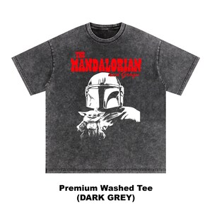Op de afbeelding: Donkergrijze premium gewassen T-shirt met een afbeelding van The Mandalorian en Grogu. Het ontwerp bevat de rode tekst "THE MANDALORIAN" boven een afbeelding van de helm van de Mandalorian en Grogu.