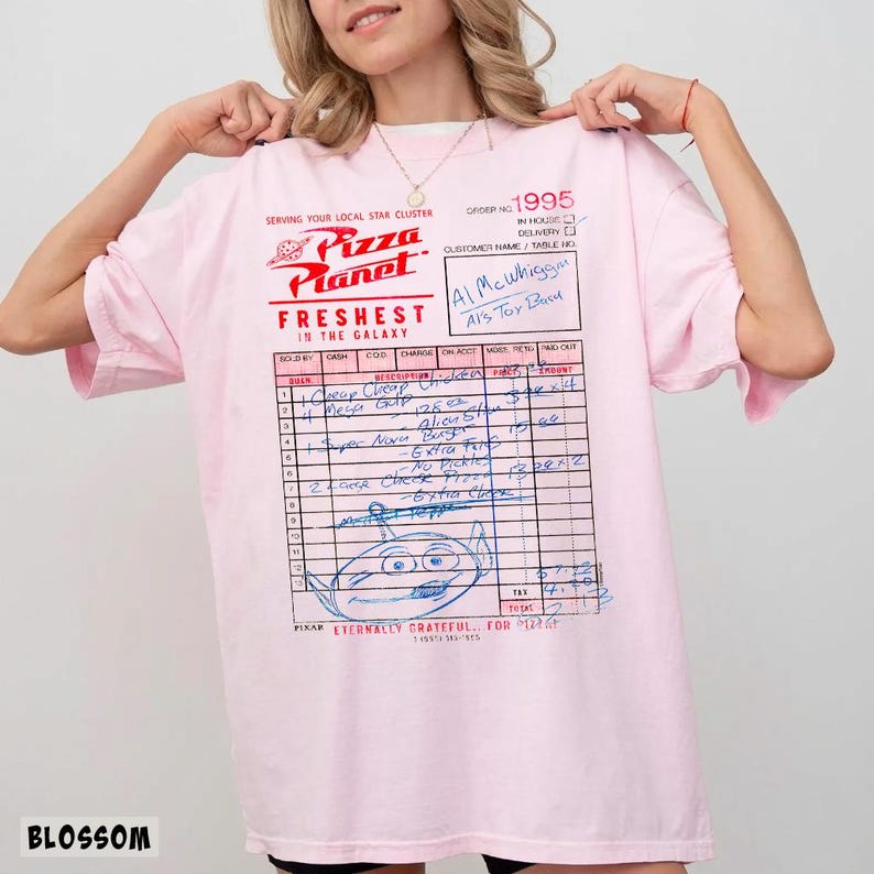 Puede incluir: Una camiseta rosa claro con un dise&ntilde;o de recibo de Pizza Planet. La camiseta incluye el logotipo de Pizza Planet, el texto "Freshest in the Galaxy" y un recibo escrito a mano con varios art&iacute;culos y el texto "Al McWhiggin, Al's Toy Barn."