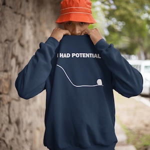 May include: Navy blue sweatshirt with the text "I HAD POTENTIAL" in white. A white line and dot graphic is below the text. The person in the image is wearing an orange bucket hat.