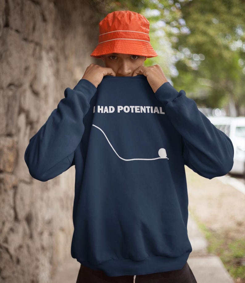 May include: Navy blue sweatshirt with the text "I HAD POTENTIAL" in white. A white line and dot graphic is below the text. The person in the image is wearing an orange bucket hat.