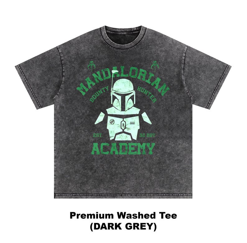 Peut inclure: T-shirt gris fonc&eacute; d&eacute;lav&eacute; avec un motif vert. Le motif comprend les mots "MANDALORIAN BOUNTY HUNTER ACADEMY" et une illustration d'un casque et d'une armure Mandaloriens. Le t-shirt est &eacute;tiquet&eacute; "Premium Washed Tee (DARK GREY)".