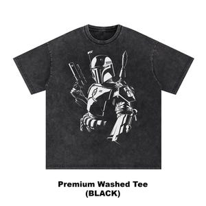 May include: Black washed tee featuring a white graphic of a helmeted character holding a blaster and a spear. The text "Premium Washed Tee (BLACK)" is printed at the bottom of the shirt. The tee has a crew neck and short sleeves.