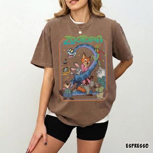 以下が含まれることがあります： 茶色のTシャツ。アニメ映画「ズートピア」のカラフルなグラフィックが特徴です。レトロなスタイルで、さまざまな動物のキャラクターと映画のタイトルが描かれています。ゆったりとしたフィット感で、半袖です。