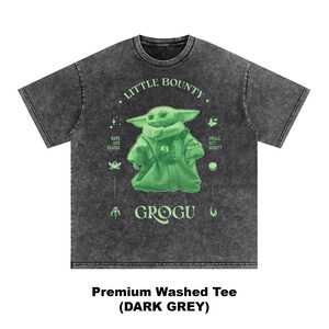 Op de afbeelding: Donkergrijs T-shirt met een groene Grogu-afbeelding. Het shirt heeft de tekst "Little Bounty" en "Grogu", samen met andere kleine afbeeldingen. Het shirt is gelabeld "Premium Washed Tee (DARK GREY)".