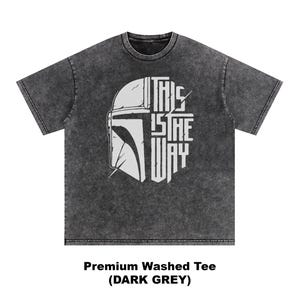 May include: Dark grey t-shirt with a white graphic of a helmet and the text "THIS IS THE WAY." The shirt is a premium washed tee in dark grey.