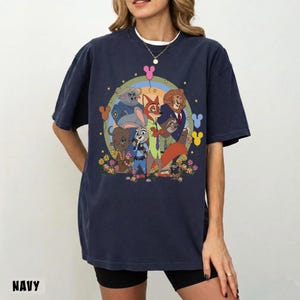May include: Navy blue t-shirt featuring a colorful graphic of animated animal characters. The design includes a rainbow, flowers, and Mickey Mouse-shaped balloons. The word "NAVY" is printed at the bottom of the shirt.