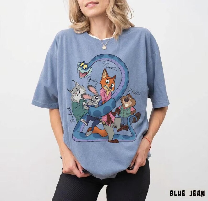 May include: A light blue t-shirt featuring a cartoon graphic of several animal characters, including a fox, rabbit, and beaver, with the number "2" formed by a blue snake. The shirt has the words "BLUE JEAN" printed at the bottom.