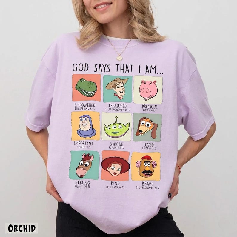 May include: A light purple t-shirt with the text "GOD SAYS THAT I AM..." and cartoon character graphics. The shirt features the word "ORCHID" at the bottom. The graphics include a dinosaur, cowboy, pig, and other characters with positive affirmations.