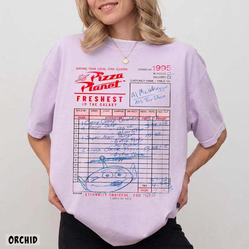 Puede incluir: Camiseta color orqu&iacute;dea con un dise&ntilde;o de recibo de Pizza Planet. El recibo incluye detalles manuscritos, un dibujo de un extraterrestre y el texto "FRESHEST IN THE GALAXY". La camiseta tambi&eacute;n tiene el logo de Pizza Planet.