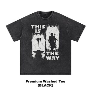 May include: Black washed tee featuring a white graphic with the text "THIS IS THE WAY" and images of a spaceship, a character with a weapon, and a silhouette of a character. The shirt is a premium washed tee.