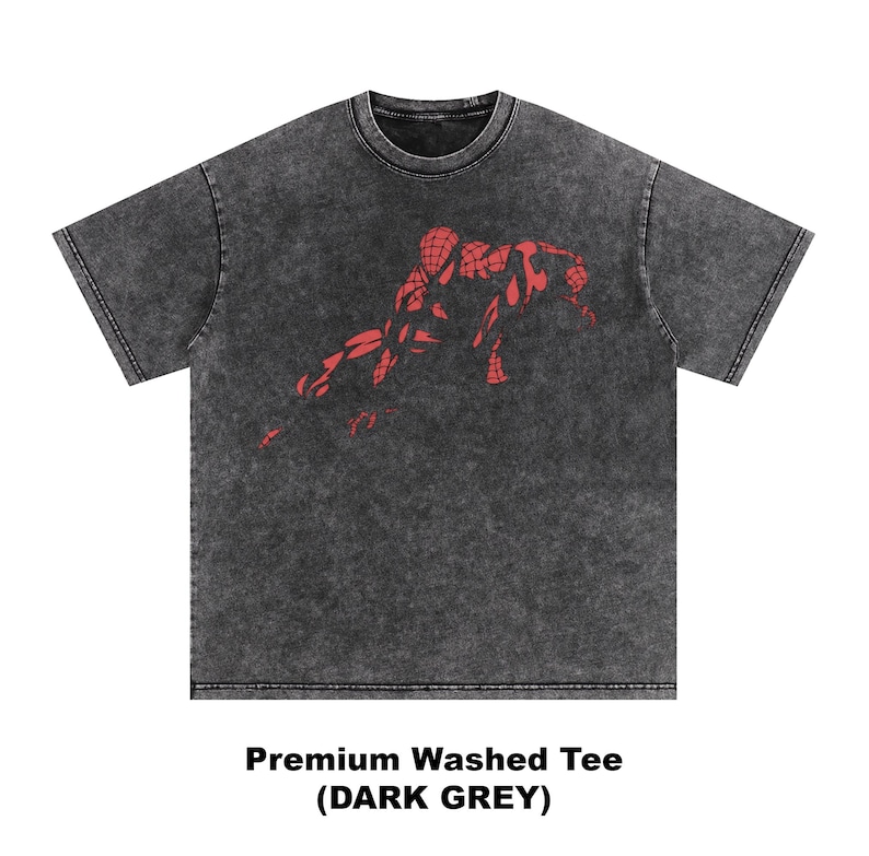 May include: A dark grey short-sleeve t-shirt with a washed, mottled texture. The center of the chest features a red graphic print of a crouching superhero figure with a webbed pattern. The text below the shirt reads Premium Washed Tee (DARK GREY).