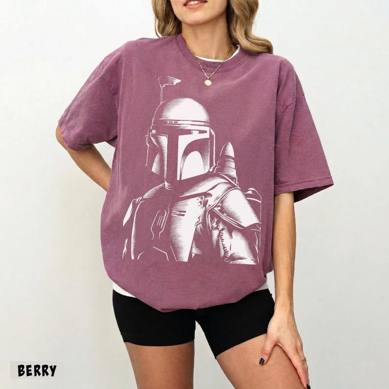 K&ouml;nnte beinhalten: Beerenfarbenes T-Shirt mit einer wei&szlig;en Grafik eines Helmkopfes. Das Shirt hat kurze &Auml;rmel und eine lockere Passform. Das Wort "BERRY" ist unten links im Bild aufgedruckt. Das Shirt wird von einer Person getragen.