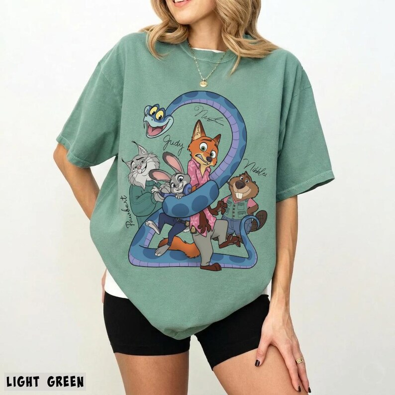 May include: Light green t-shirt featuring a cartoon graphic of several animal characters, including a fox, rabbit, and beaver, with the number 2 and the names of the characters. The text "LIGHT GREEN" is at the bottom.