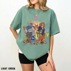 May include: Light green t-shirt featuring a colorful graphic of Zootopia characters. The design includes Judy Hopps, Nick Wilde, and other characters in a circular arrangement with flowers and balloons. The text "LIGHT GREEN" is at the bottom.