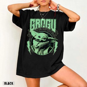 May include: Black t-shirt featuring a green graphic of Grogu, with the name "GROGU" above the image. The design includes lightning bolts and flames. The word "BLACK" is printed at the bottom left of the shirt.