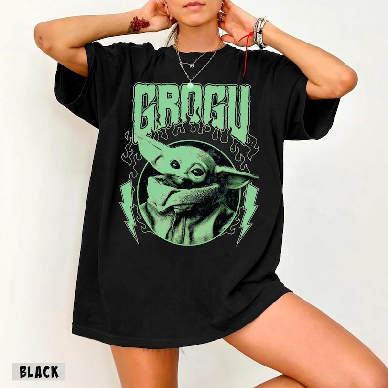 May include: Black t-shirt featuring a green graphic of Grogu, with the name "GROGU" above the image. The design includes lightning bolts and flames. The word "BLACK" is printed at the bottom left of the shirt.