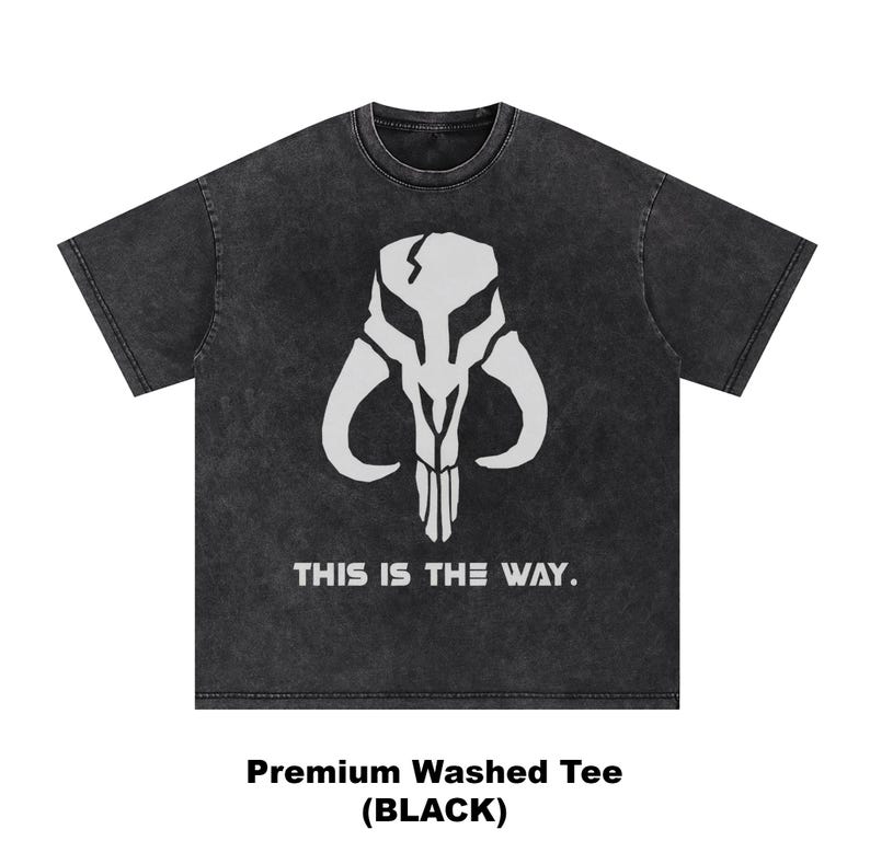 May include: Black washed tee featuring a white graphic of a skull-like helmet with the text "THIS IS THE WAY." The shirt is a premium washed tee.