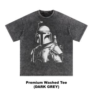 K&ouml;nnte beinhalten: Dunkelgraues, ausgewaschenes T-Shirt mit einer wei&szlig;en Illustration einer Figur mit Helm. Die Grafik ist mittig auf der Vorderseite platziert. Der Text "Premium Washed Tee (DARK GREY)" ist darunter gedruckt.