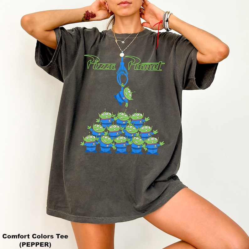May include: Dark gray t-shirt featuring the Pizza Planet logo in green and a graphic of the Little Green Men from Toy Story. The shirt has a relaxed fit and a vintage look, perfect for fans of the animated film.