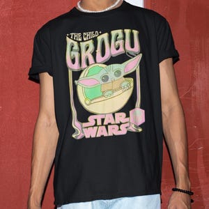 May include: Black t-shirt featuring a Grogu graphic from Star Wars. The design includes the text "THE CHILD GROGU" in pink and green, with Grogu in a pod. The Star Wars logo is at the bottom.