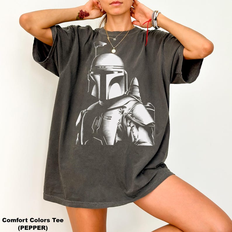 K&ouml;nnte beinhalten: Dunkelgraues Comfort Colors T-Shirt mit einer wei&szlig;en Grafik eines Helmtr&auml;gers. Das Bild ist eine detaillierte Illustration der R&uuml;stung und des Helms der Figur. Der Text "Comfort Colors Tee (PEPPER)" befindet sich am unteren Rand des Shirts.