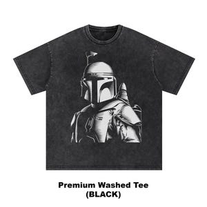 K&ouml;nnte beinhalten: Schwarz gewaschenes T-Shirt mit einer wei&szlig;en Illustration eines behelmten Charakters. Die Grafik ist detailliert und stilisiert. Der Text "Premium Washed Tee (BLACK)" ist unten auf dem T-Shirt aufgedruckt.